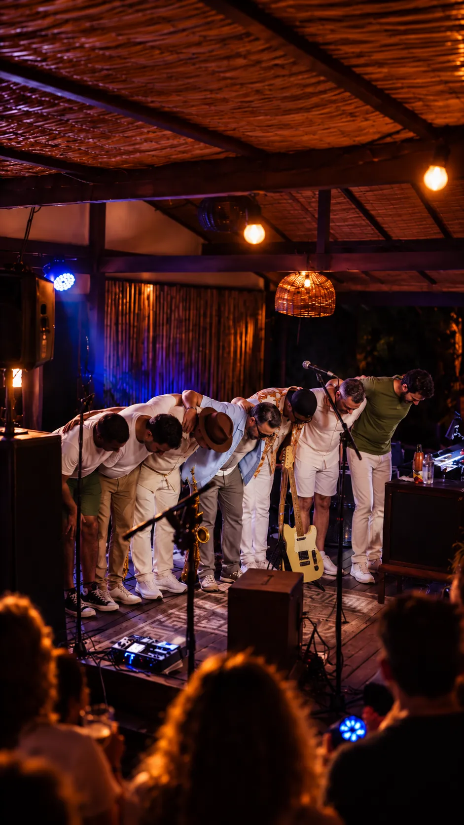 A banda curvada em agradecimento ao público, num palco coberto e iluminado.