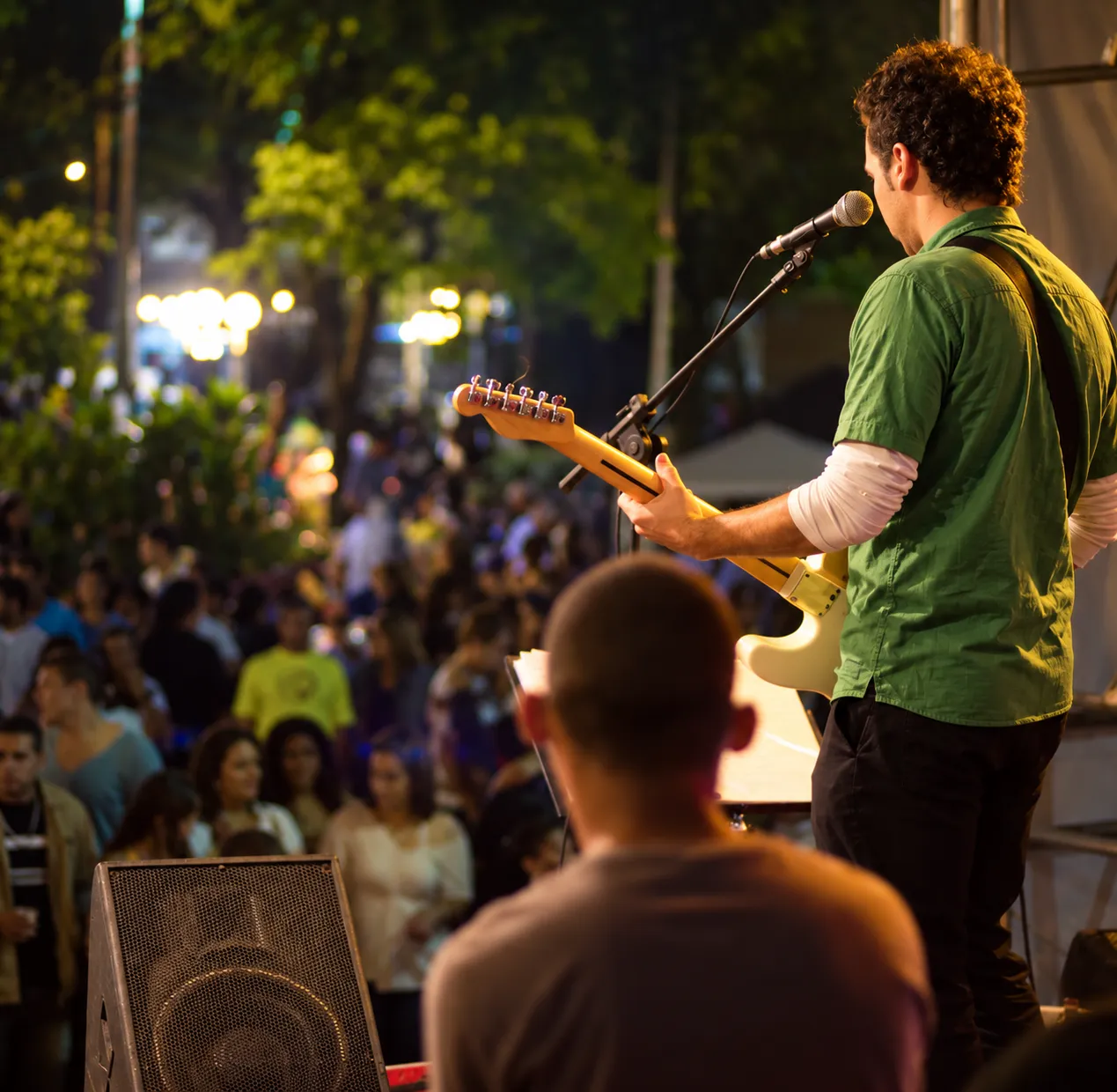 Pablo Curty tocando guitarra num palco ao ar livre, de frente para o público na rua.