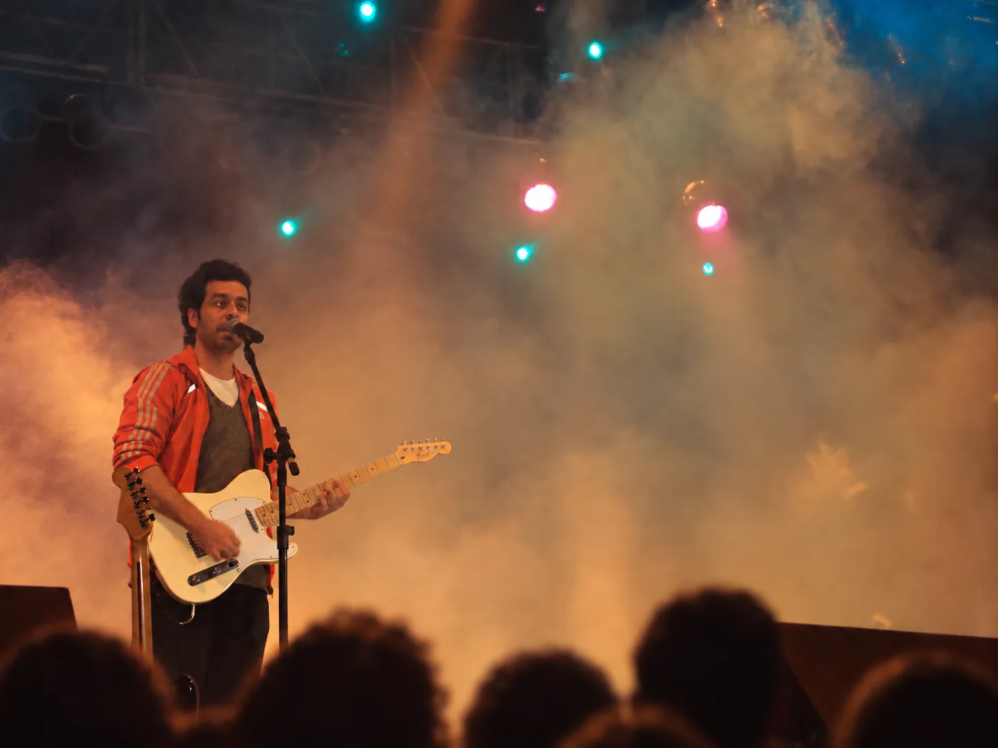 Pablo Curty cantando e tocando guitarra num palco com fumaça e luzes coloridas.