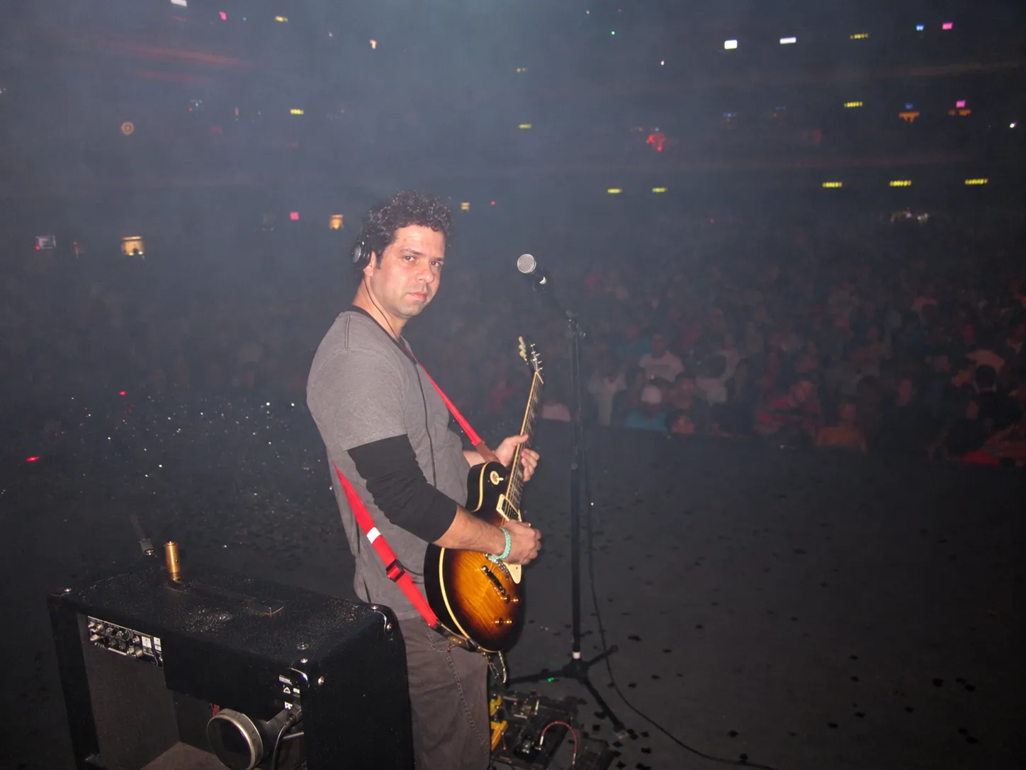 Pablo Curty com guitarra no palco, de costas para uma arena cheia.